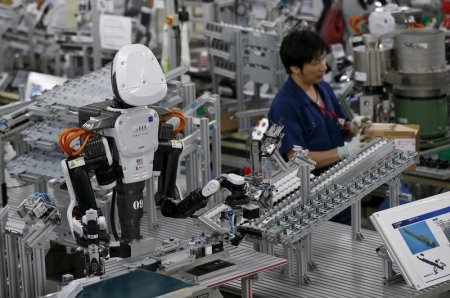 A humanoid robot works side by side with employees in the assembly line at a factory of Glory Ltd. a manufacturer of automatic change dispensers in Kazo north of Tokyo Japan