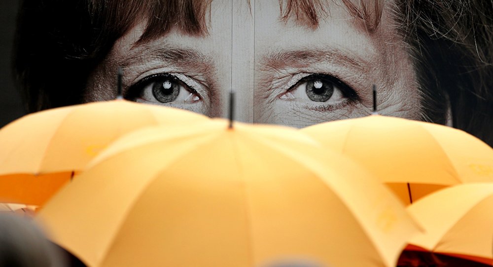 Supporters of the Christian Democratic Union hold umbrellas in front of a giant portrait of German Chancellor Angela Merkel during an election campaign event in front of the party's headquarter in Berlin Germany Monday Sept. 16 2013