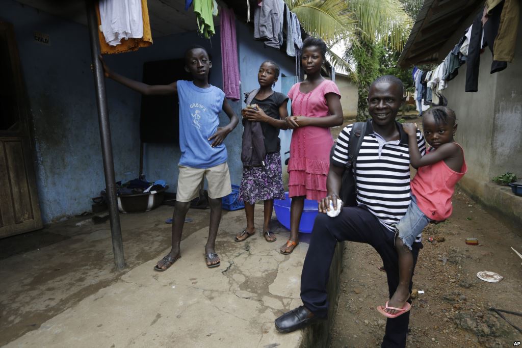 FILE- Laboratory technician Mohamed SK Sesay who survived Ebola but saw many of his colleagues die and now has joint and muscle pains and loss of sight holds the child of one of his work colleagues who died of the disease in Kenema Sierra Leone Aug