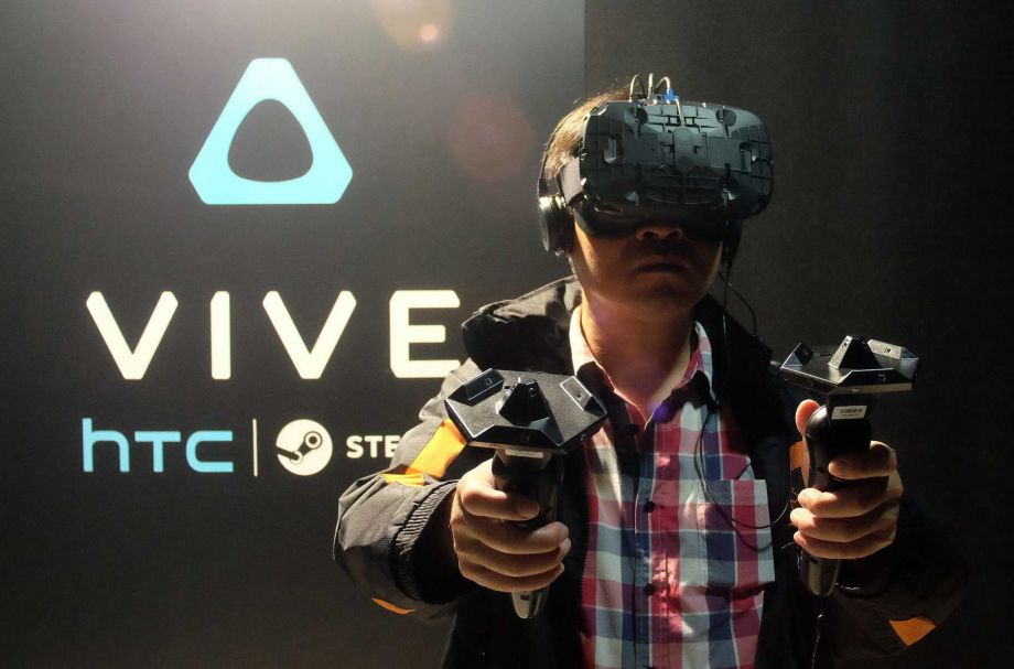 A fan wears a HTC Vive headset and holds two sensors during a promotional event held by HTC in Taipei last month. Smartphone maker HTC unveiled to Taiwanese gamers its virtual reality headset for the first time as the company pins hopes on the new produc