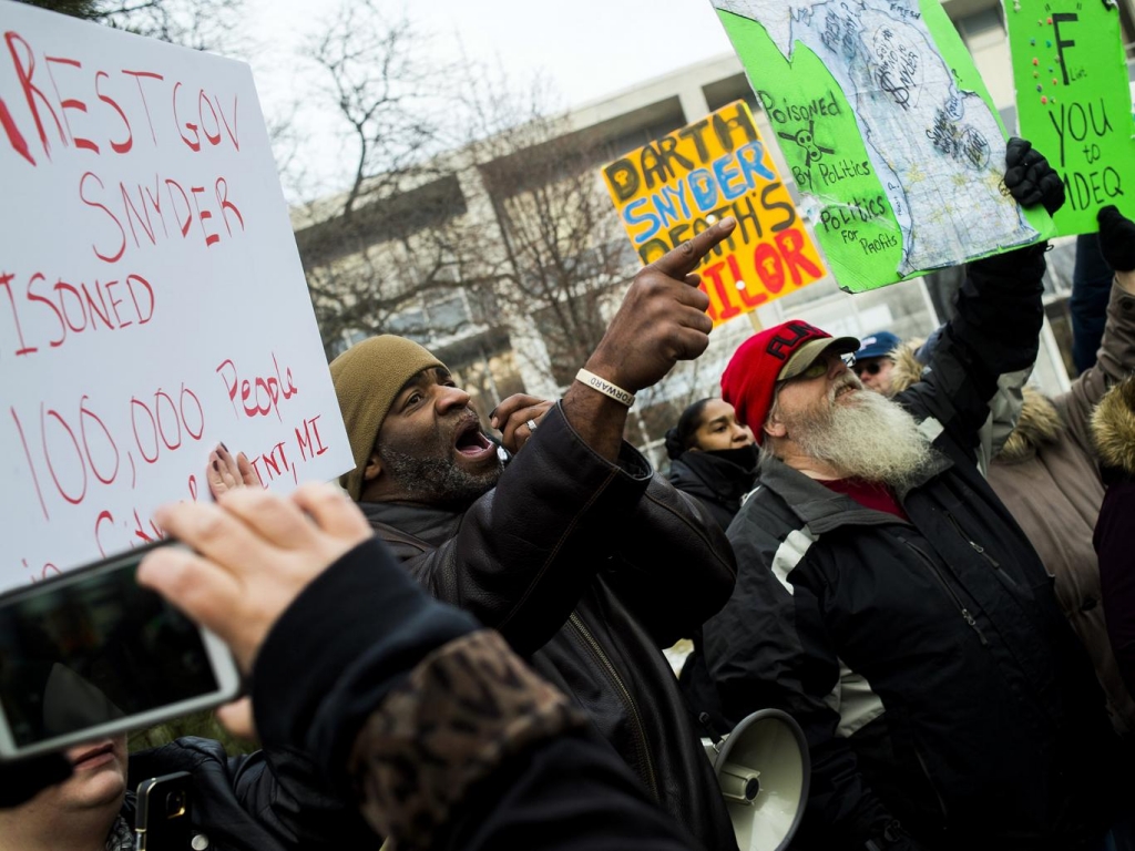 Flint Michigan residents Arthur Woodson left and Tony Palladino Jr. protest the arrival of Flint native and filmmaker Michael Moore as Moore accuses Gov. Rick Snyder of poisoning Flint water during a rally outside of city hall in Flint Mich