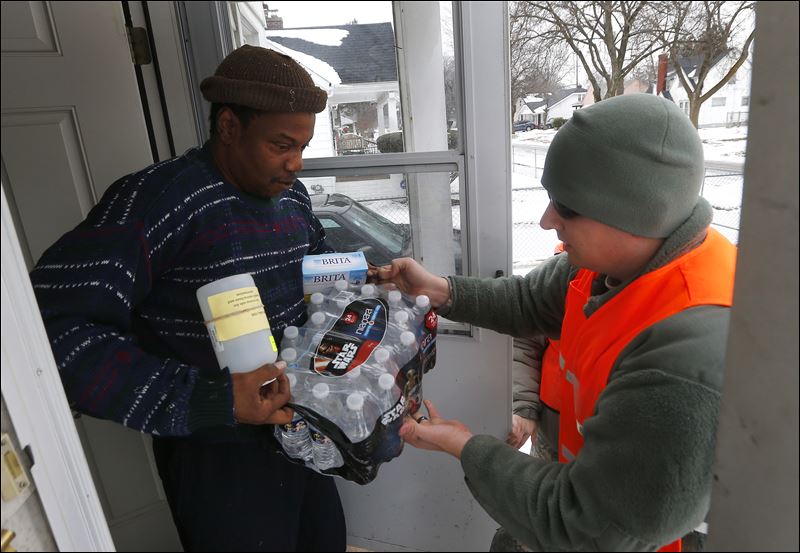 Louis Singleton receives water filters bottled water and a test kit from Michigan National Guard Specialist Joe Weaver as clean water supplies are distributed to residents in Flint