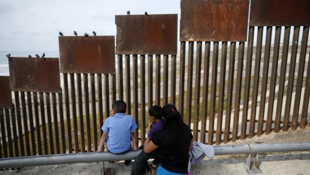 A family looks towards metal bars marking the United States border where it meets the Pacific Ocean in Tijuana Mexico