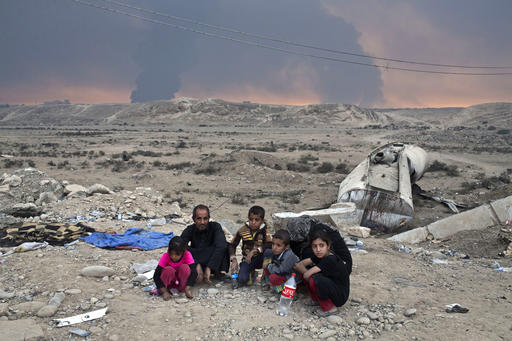 Internally displaced persons sit at a checkpoint as smoke rises from the burning oil wells in Qayyarah about 31 miles south of Mosul Iraq Sunday Oct. 23 2016. Islamic State fighters torched a sulfur plant sou