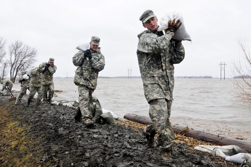 U.S. Army Spcs. Eric Wiederholt, Joshua Lanzdorf and Randy Birchfield carry sandbags in the rain along a flood levee for placement on a flood barrier in a rural farmstead in Cass County N.D