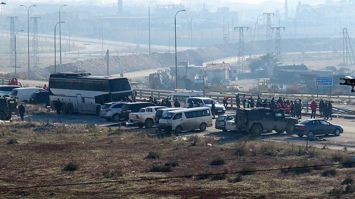 People wait next to vehicles as a convoy of four buses arrives at the Syrian government-controlled crossing of Ramoussa