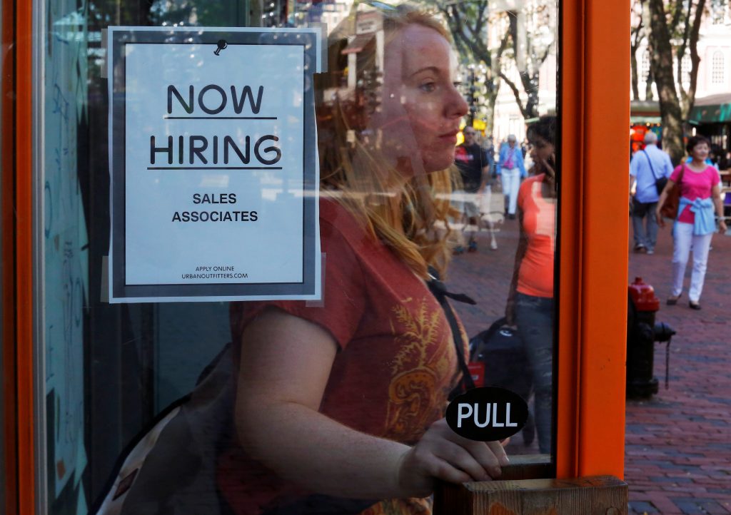 A woman walks past a'Now Hiring sign as she leaves the Urban Outfitters store at Quincy Market in Boston Massachusetts