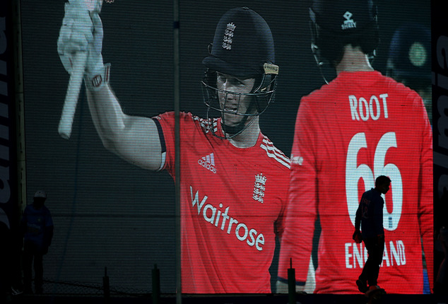 An Indian spectator walks in front of a giant screen showing England's captain Eoin Morgan celebrating his fifty runs during their first Twenty20 cricket mat