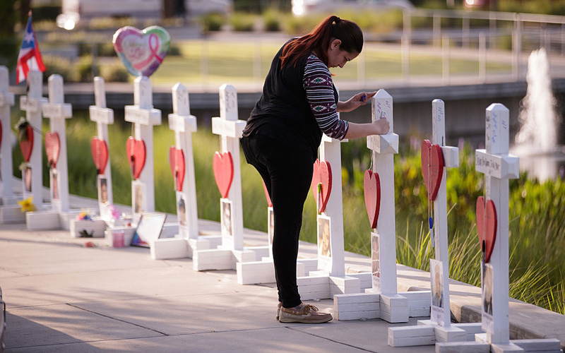 A woman writes a note on a cross at a memorial with wooden crosses for each of the 49 victims of the Pulse Nightclub next to the Orlando Regional Medical Center