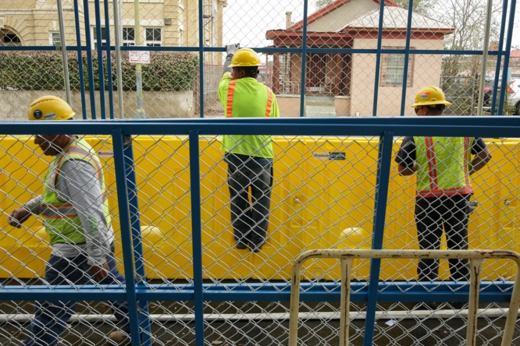 Workers of Waterfilled Barrier Systems assembly a fence and barrier along Travis Street