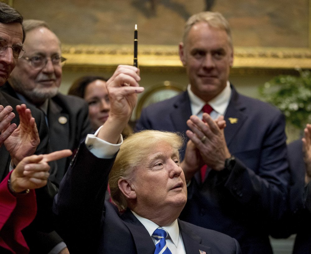 President Trump holds up the pen he used to sign a bill in the Roosevelt Room of the White House on Monday. From left are Sen. Tom Barrasso R-Wyo. Rep. Don Young R-Alaska and Interior Secretary Ryan Zinke