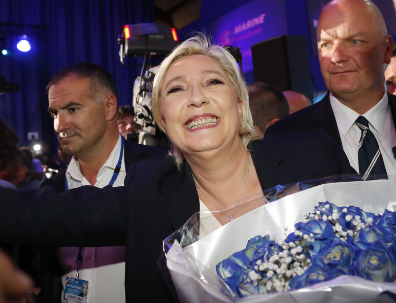 Far-right leader and candidate for the 2017 French presidential election Marine Le Pen surrounded by bodyguards celebrates with supporters while holding a bunch of flowers after exit poll results of the first round of the presidential election were ann