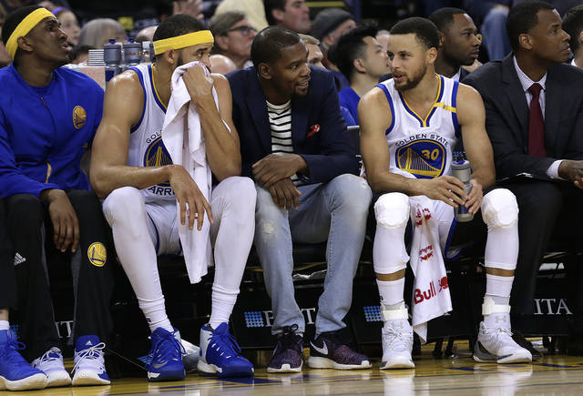 Golden State Warriors&#039 Kevin Durant center sits on the bench between Stephen Curry and Ja Vale McGee second from left during the first half of the team's NBA basketball game against the Sacramento Kings on Friday in Oakland Calif. Duran