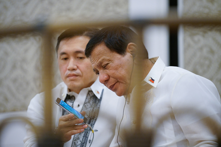 President Rodrigo Roa Duterte is assisted by Special Assistant to the President Christopher Lawrence Go as he speaks to US President Donald Trump through a phone call on the sidelines of the gala dinner hosted by President Duterte for the Head of States