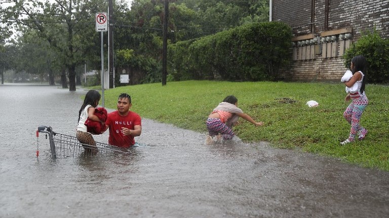 A man helps children across a flooded street as they evacuate their home in Houst