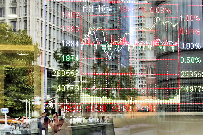 People and office buildings are reflected on a brokerage house’s window as an electronic board displaying stock trading index in Beijing. – AP