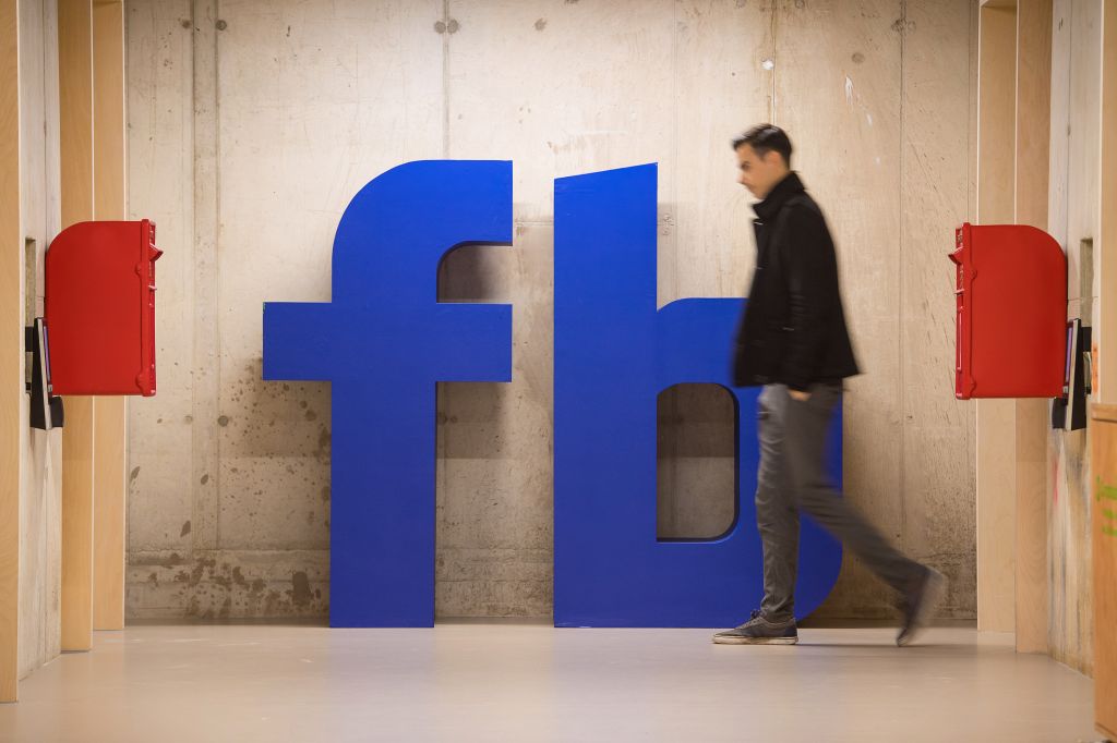 A man walks past a Facebook logo at Facebook's Frank Gehry-designed headquarters at Rathbone Place in London