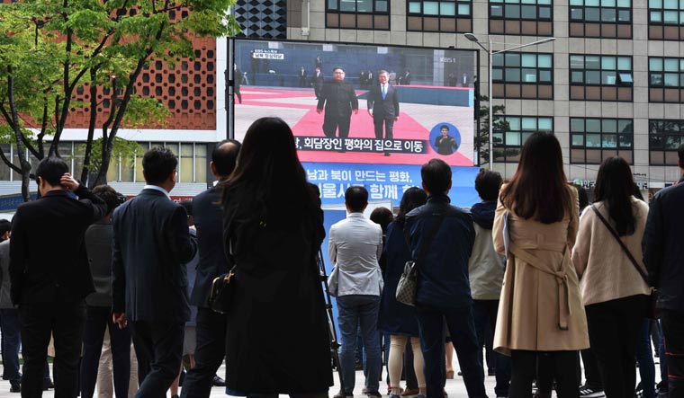 People watch live footage of South Korean President Moon Jae-in walking with North Korean leader Kim Jong Un at the Demilitarized Zone on a screen in Seoul | AFP